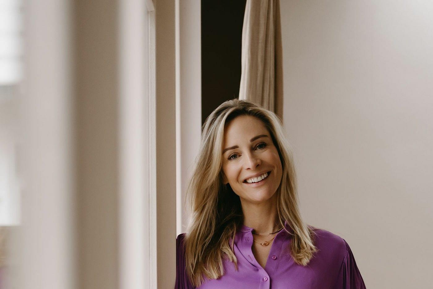 Virginie Versteegh in een paars pak, staand bij een raam
