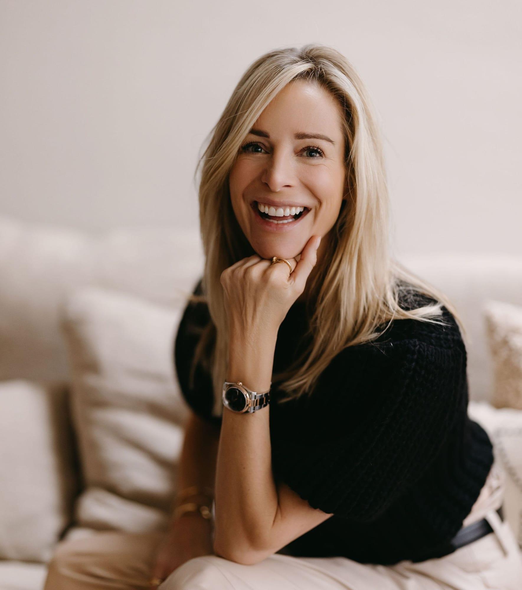 Virginie Versteegh in een zwarte top, lachend op een lichte bank