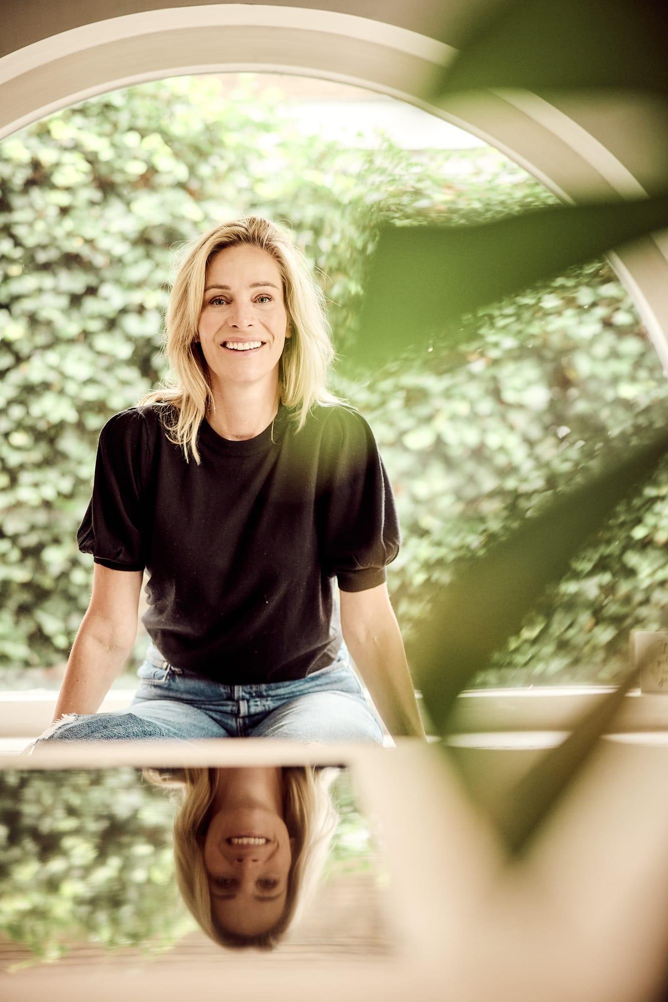 Virginie Versteegh in een zwart shirt, zittend in een ronde raamopening met groen
