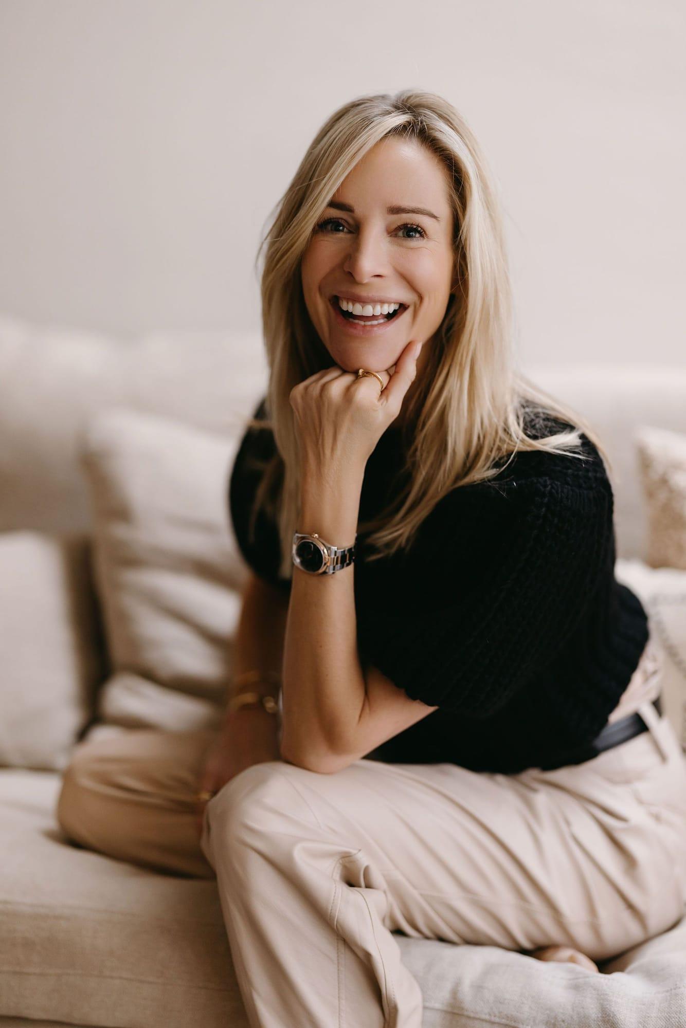 Virginie Versteegh in een zwarte top op een bank, lachend met haar hand aan haar kin