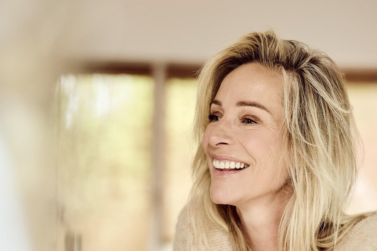 Virginie Versteegh in een beige vest, lachend aan de keukentafel