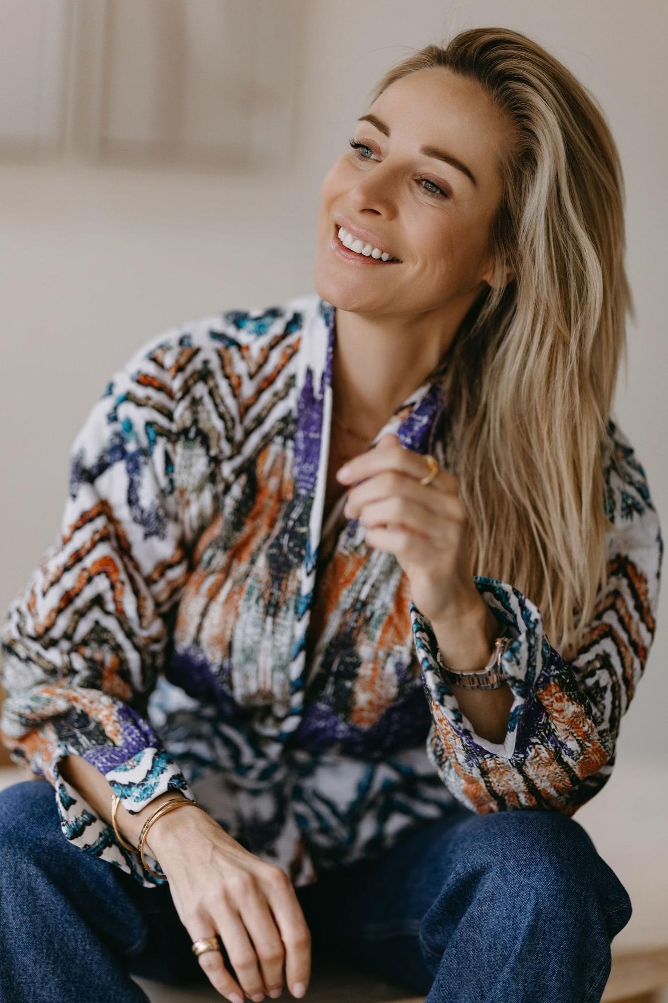 Virginie Versteegh in een kleurrijke blouse, zittend en lachend