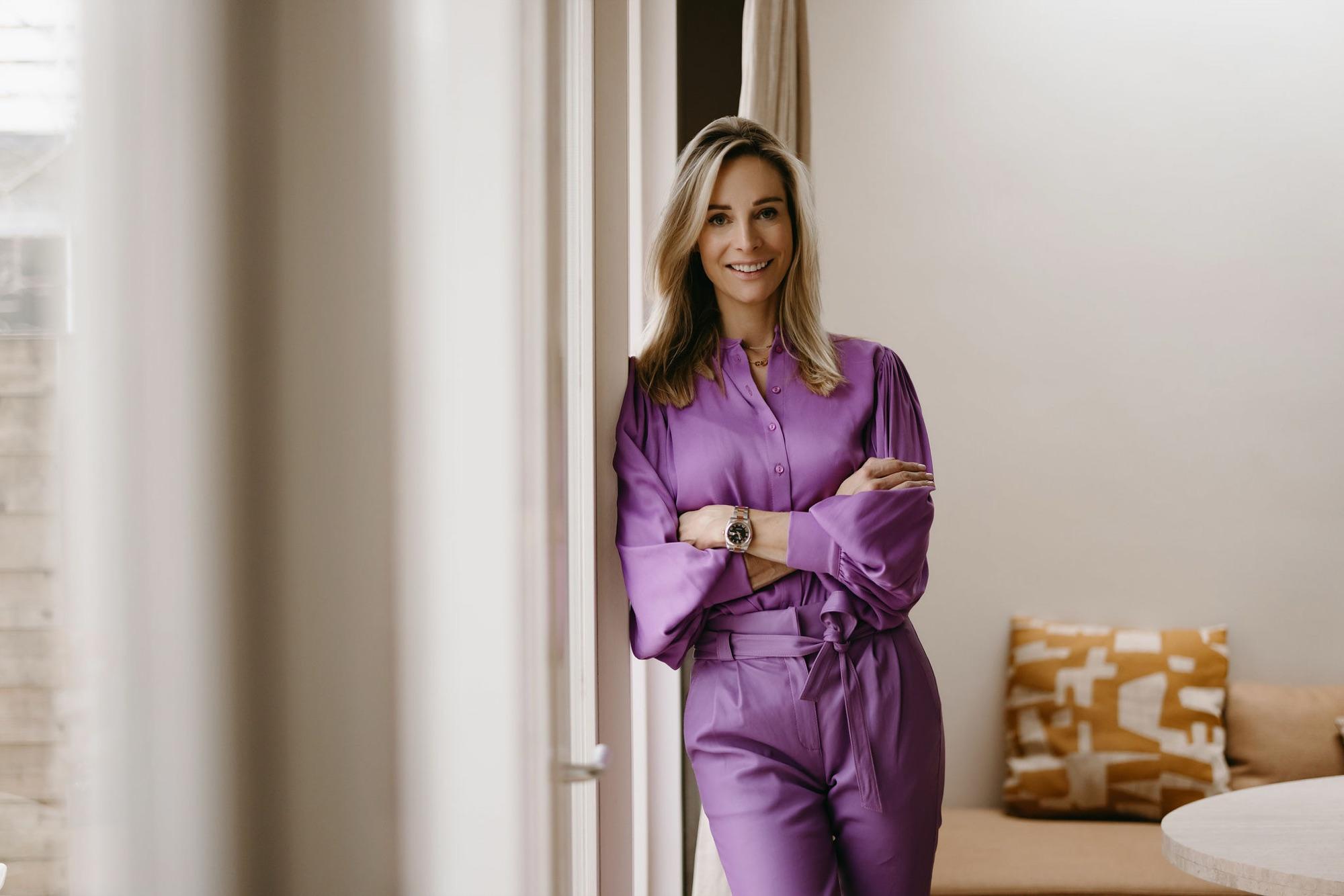 Virginie Versteegh in een paars pak, staand bij het raam met de armen over elkaar